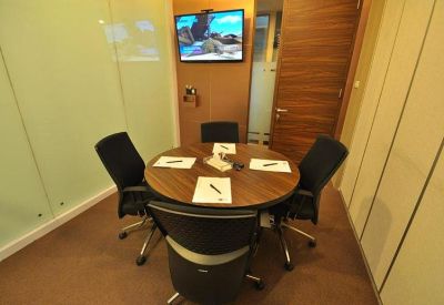 Small round wooden meeting table with four black mesh chairs in a bright office.