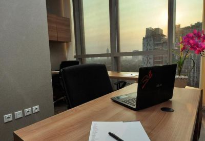 Close-up of a wooden desk with a laptop and branded notepad overlooking a city sunset.