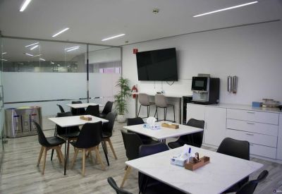 Kitchen and breakout area with white tables, black chairs, and coffee machine.