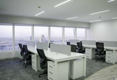 Bright workspace with rows of desks and panoramic city views through large windows.