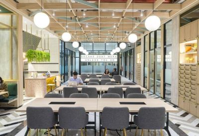 Open-plan coworking area with rows of gray chairs, large desks, and globe pendant lighting.