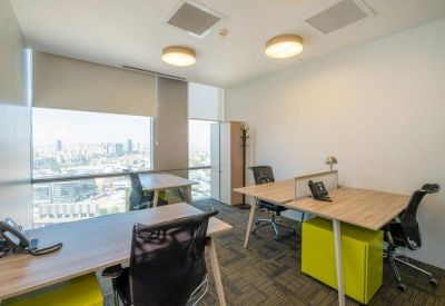 Bright private office featuring three wooden desks and floor-to-ceiling windows with city views.
