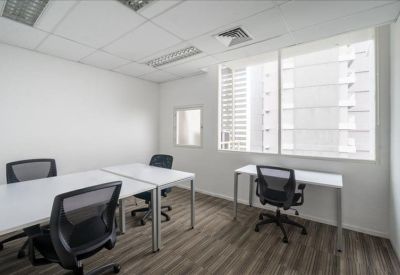 Bright corner office with three white desks and ergonomic black mesh chairs.