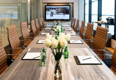 Sophisticated boardroom with a long wood-grain table, leather chairs, and white flower arrangements.