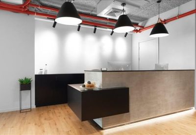 Modern reception desk with wood flooring, red ceiling pipes, and black pendant lights.