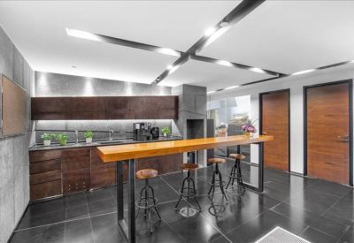 Modern office kitchen area with a high breakfast bar, dark cabinetry, and sleek cross-lighting.