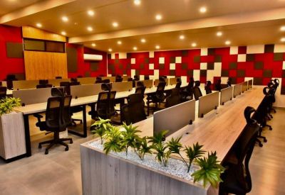 Open-plan office with rows of wooden desks, ergonomic chairs, and red accent walls.