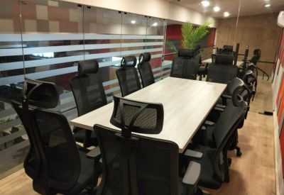 Modern conference room with a light wood table and black mesh chairs behind glass partitions.