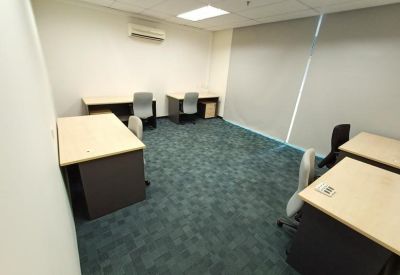 Open-plan office space featuring four light wood desks on teal carpeting.