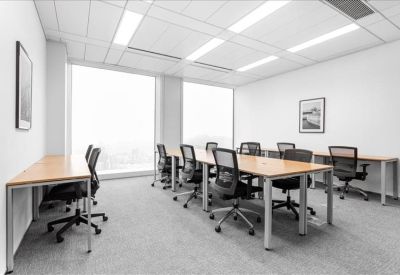Bright open-plan workspace with multiple wooden desks and black mesh chairs.