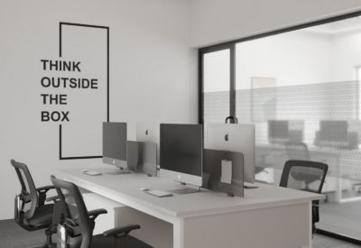 Open-plan office with white desks, black ergonomic chairs, and Think Outside the Box wall art.
