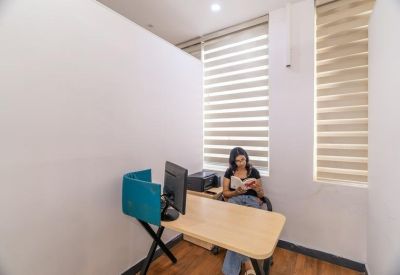 Private office pod with a wooden desk and a person reading near window blinds.
