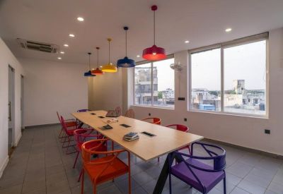 Natural light-filled meeting room with a large table, vibrant seating, and city views through windows.