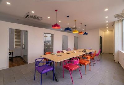 Bright shared workspace featuring a long wooden table and colorful modern chairs.
