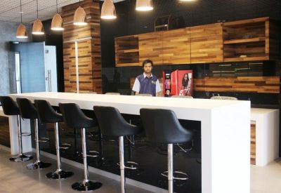 Modern office café area with a white counter, black bar stools, and wood cabinetry.