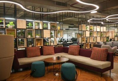 Vibrant communal lounge with a large L-shaped sofa, teal ottomans, and decorative plant shelving.