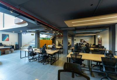 Spacious open-plan office with numerous workstations, ergonomic chairs, and dark industrial ceilings.
