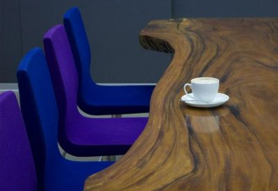 Close-up of a live-edge wooden communal table with vibrant blue and purple chairs.