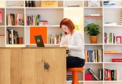 Modern office workspace featuring a woman working at a wooden desk in front of white built-in bookshelves.