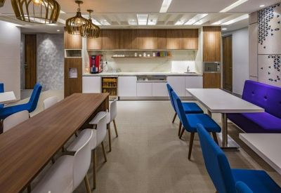 Bright breakout area featuring wood-toned dining tables, vibrant blue chairs, and a purple booth.