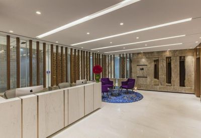 Professional reception lobby with a light wood desk, purple lounge chairs, and a blue patterned rug.