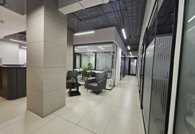 Clean office hallway leading past glass-walled suites and a waiting area with armchairs.