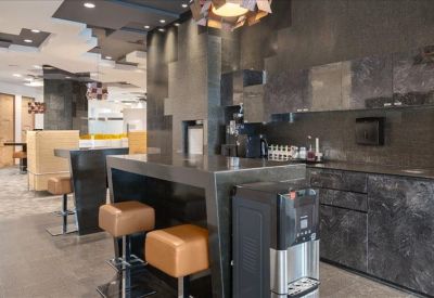 Modern office kitchen and breakout area with dark stone finishes and high stools.