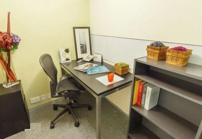 Small private office with a dark wood desk, grey ergonomic chair, and a bookshelf with colorful books.