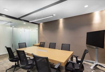 Modern meeting room with a wooden table, black mesh chairs, and a large wall-mounted screen.