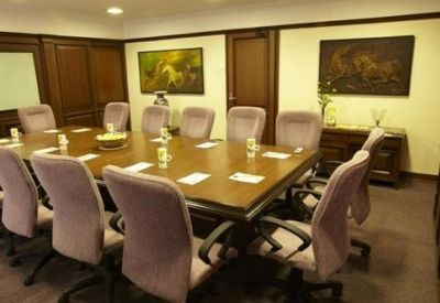 Formal boardroom with a large wooden table, plush grey chairs, and wood-paneled walls.