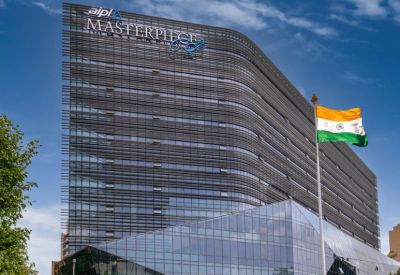 Exterior view of the glass-facade AIPL Masterpiece building with the Indian flag in the foreground.