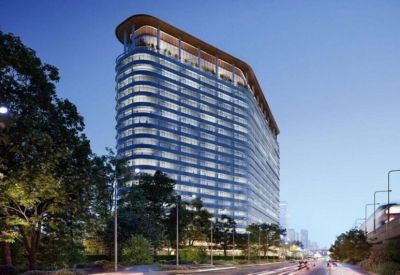 Curved glass office tower illuminated at dusk, with trees and a busy road in the foreground.