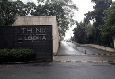 Entrance signage wall featuring the brand logo next to a paved driveway and lush green trees.