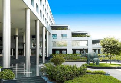 Modern building entrance with tall silver pillars, manicured gardens, and elephant sculptures.