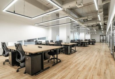 Bright open-plan workspace with wooden desks, ergonomic black chairs, and geometric LED ceiling lights.
