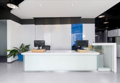 Clean white reception desk with monitors and a potted plant.