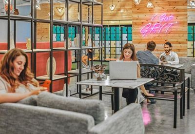 Bright workspace featuring marble-topped tables, industrial shelving, and a neon grit sign.