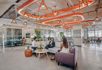 Large breakout space with unique orange ring lighting, grey sofas, and a white coffee table.