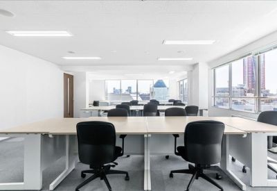 Open-plan office with multiple rows of workstations and large windows overlooking the city.