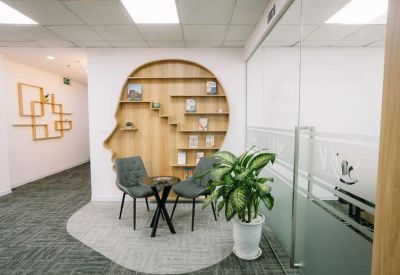 Modern lounge area with a unique head-shaped bookshelf and comfortable green chairs.