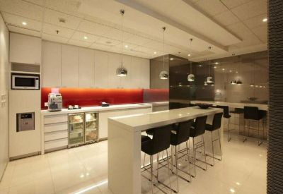 Modern communal kitchen and break area with white cabinetry and red backsplash.