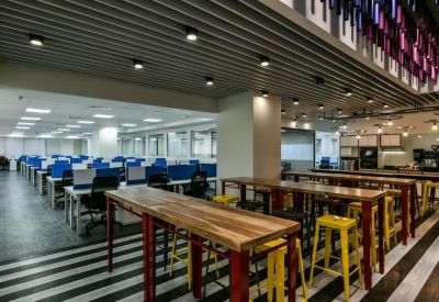Bright open-plan office featuring rows of blue workstations and high wooden collaboration tables.
