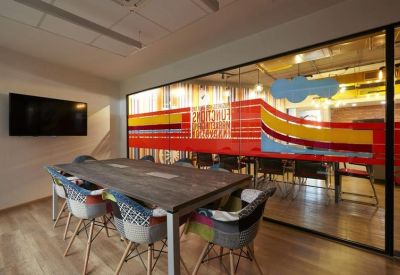 Modern meeting room with a large wooden table, patchwork chairs, and a colorful glass partition.