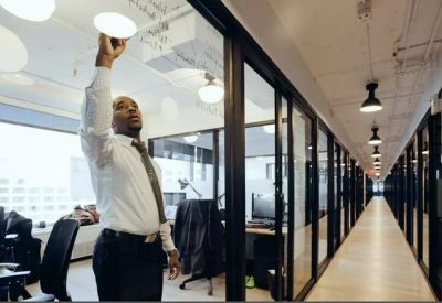 Modern hallway with glass partitions and a worker adjusting a ceiling light.