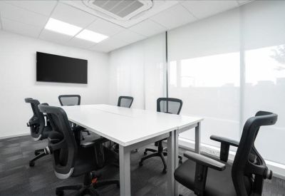 Bright conference room with a large white table, wall-mounted screen, and black seating.