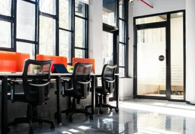 Bright open-plan office with black mesh chairs and orange privacy screens along a window wall.