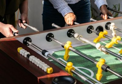Close-up of people playing foosball on a wooden table in a breakroom.
