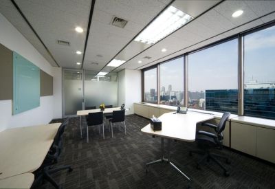 Bright open-plan office with white desks and large windows overlooking the city.