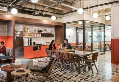 Modern communal kitchen with orange cabinetry, a long dining table, and patterned floor tiles.