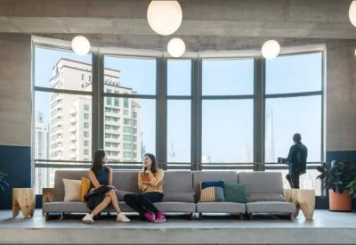 Lounge area with grey seating facing a large window with a view of a neighboring skyscraper.